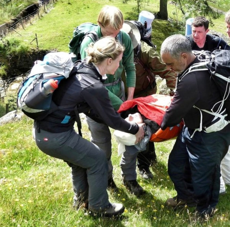 Group of people assisting a person on a stretcher in a grassy outdoor setting