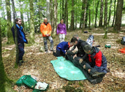 Group of people in a forest setting, with one person tending to another on a green mat.
