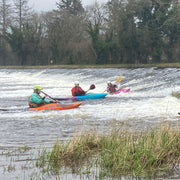 Three kayakers on a river with trees and grass in the background