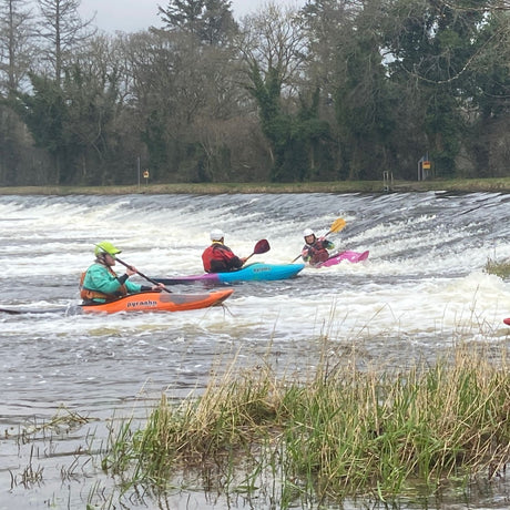 Three kayakers on a river with trees and grass in the background