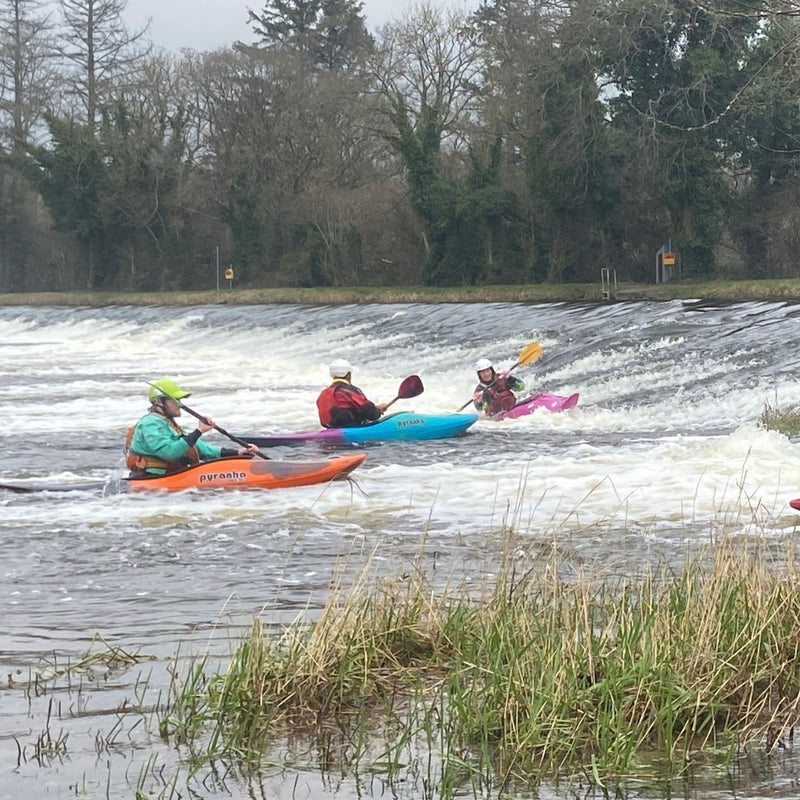 Three kayakers on a river with trees and grass in the background