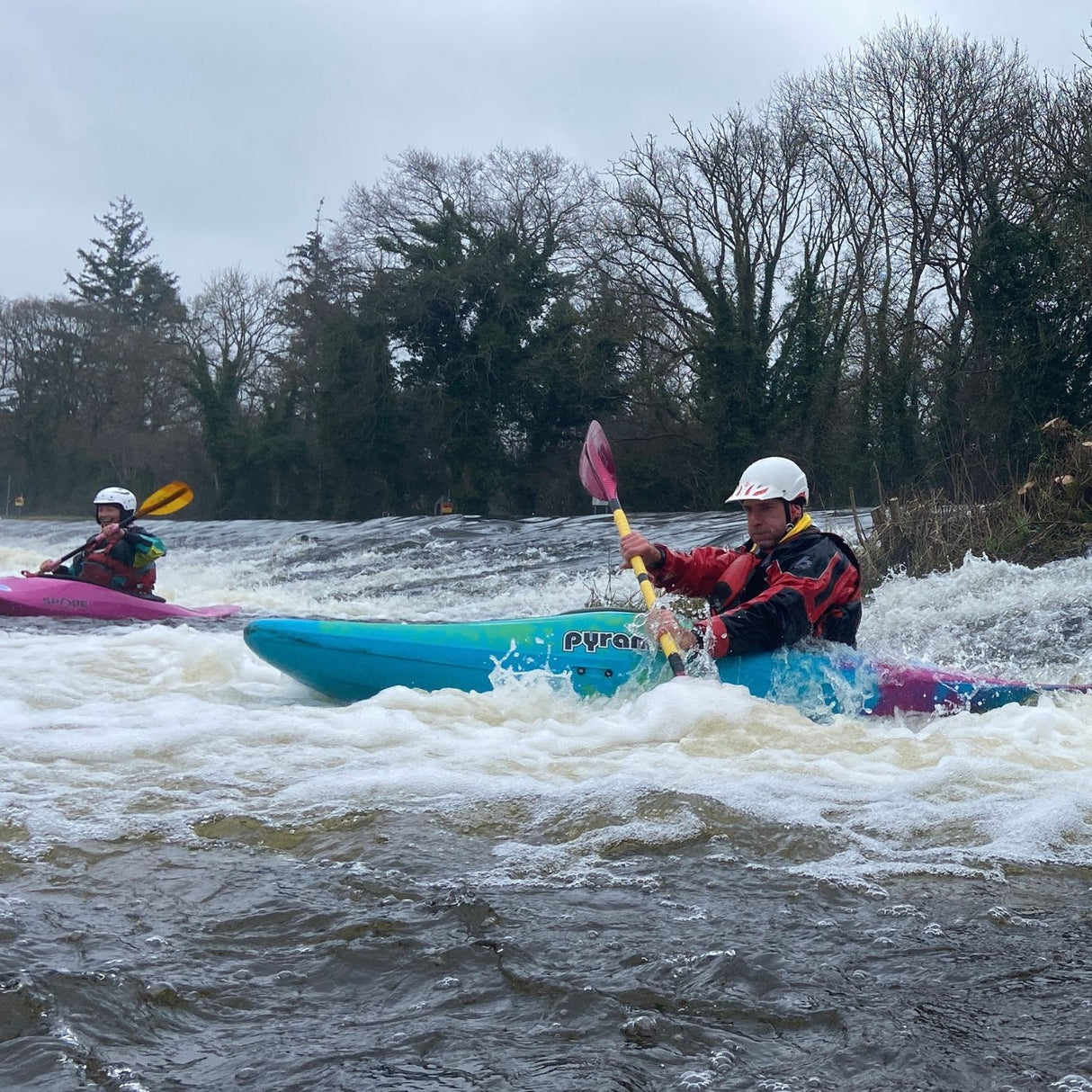 Two people kayaking on a river with trees in the background