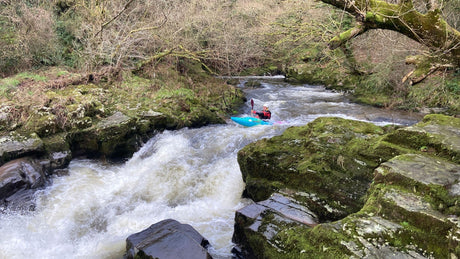 Person kayaking through a rocky river with greenery on either side